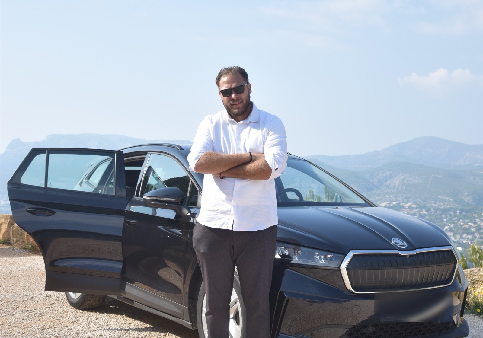La Škoda Enyaq à l'arrêt, portière arrière ouverte, sur une hauteur au-dessus de la baie